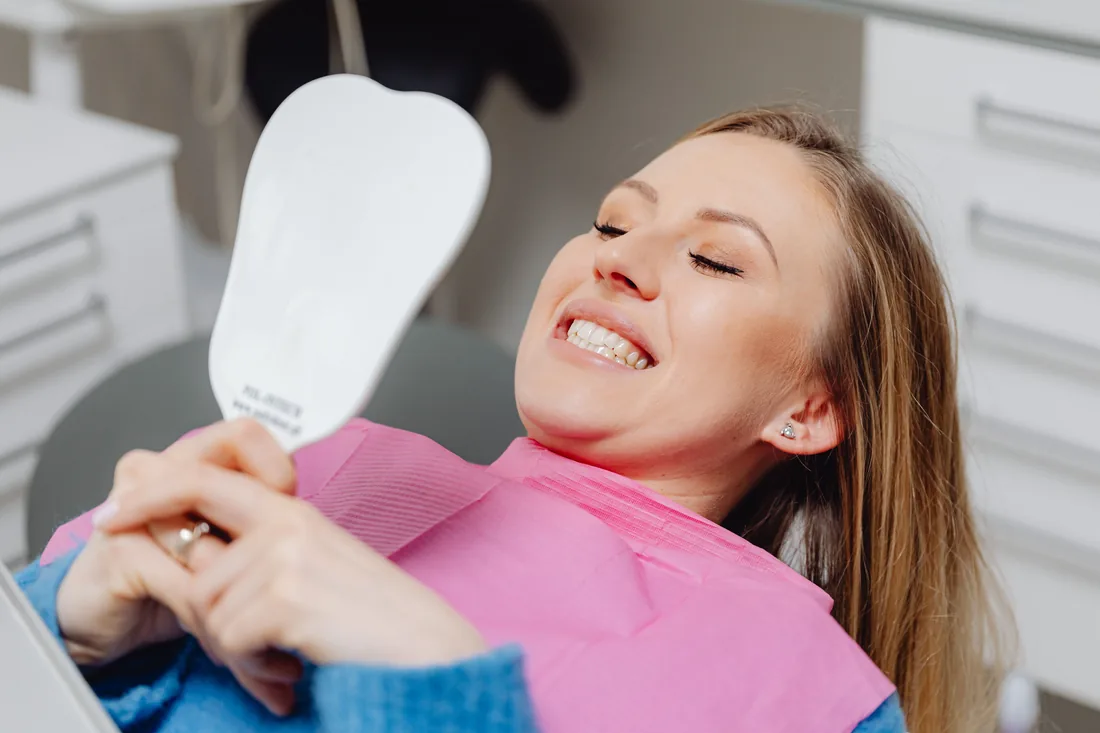 Patient smiling at her whitened teeth in a hand mirror during a dental visit